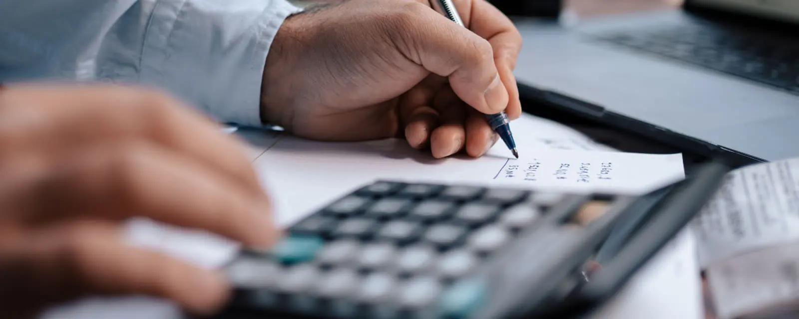 Hands using a calculator beside a laptop, illustrating the ZipNumbers calculator tools